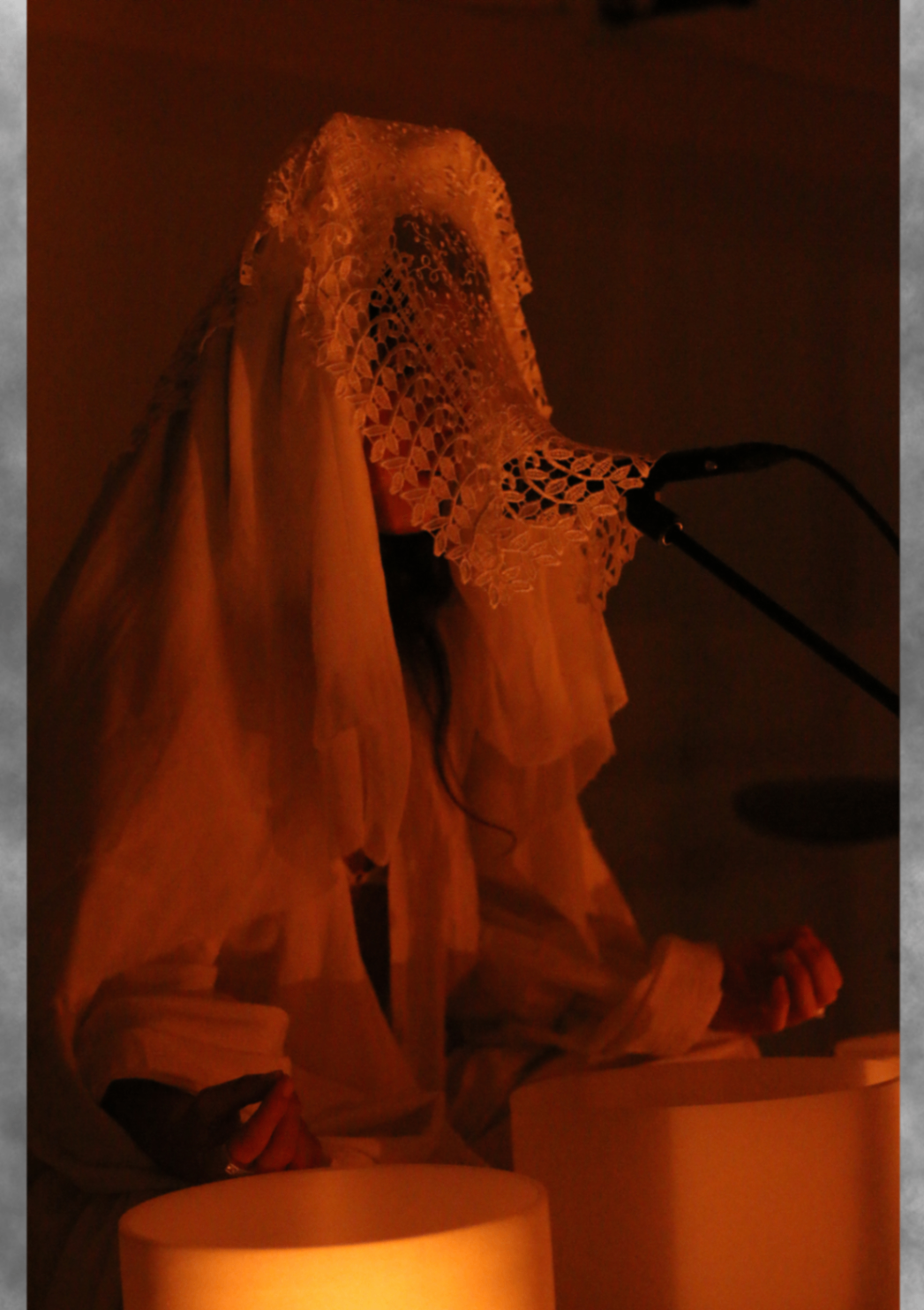 Veiled performer at illuminated crystal bowls in warm orange light.
