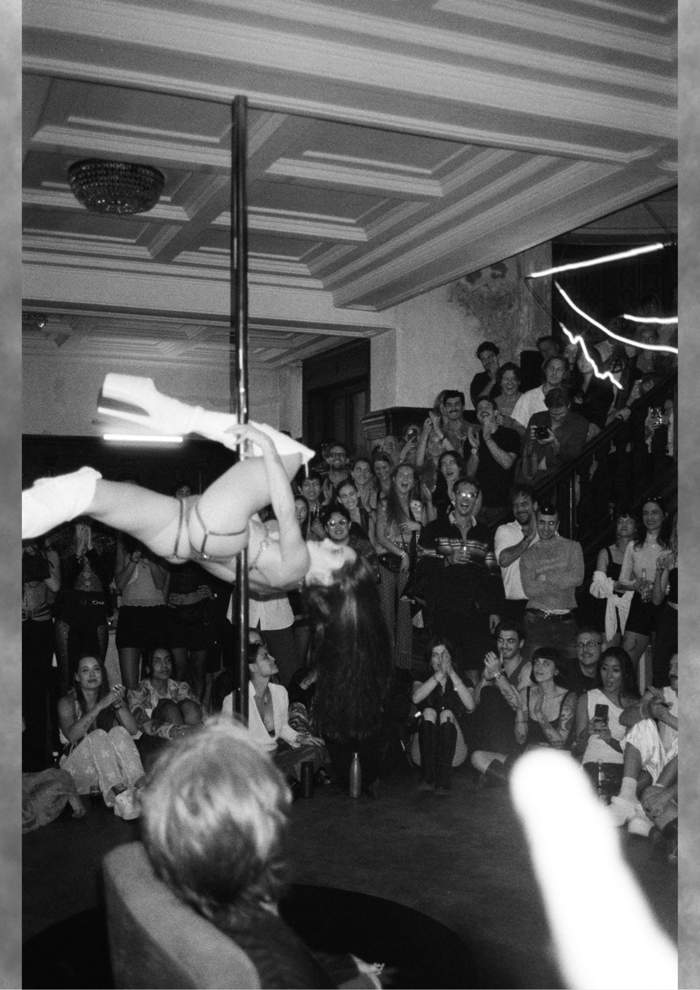 Aerial pole performer suspended above a captivated crowd in black and white.